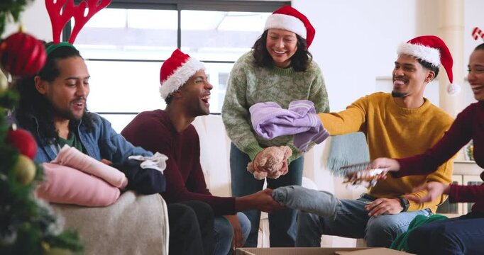At christmas, young diverse friends wearing festive hats packing clothes for donations at home