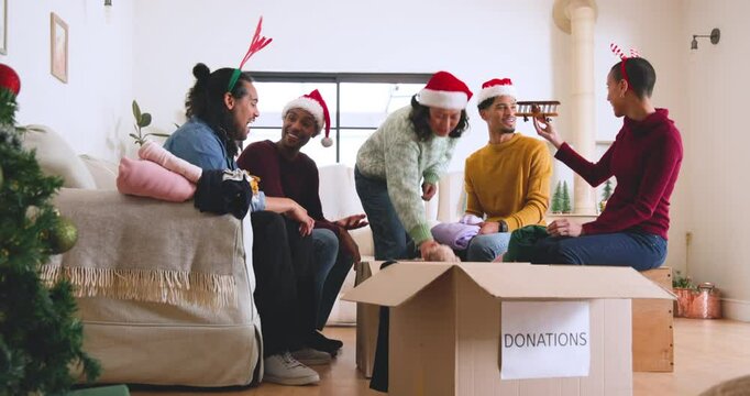 At christmas, young diverse friends wearing festive hats packing clothes for donations at home