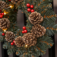 A festive Christmas wreath adorned with pine cones, red berries, and warm white fairy lights