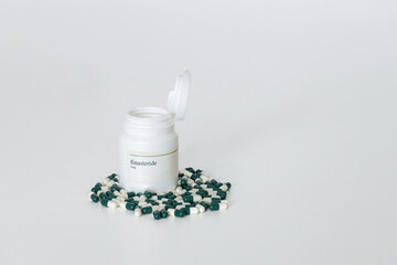 1mg finasteride pill bottle with spilled capsules on a white surface. Hair loss treatment medication
