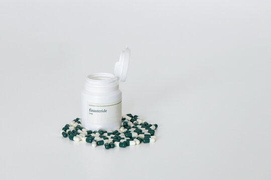 1mg finasteride pill bottle with spilled capsules on a white surface. Hair loss treatment medication