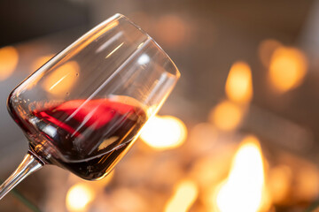 A glass of red wine captures the soft glow from a nearby fire, enhancing the mood with subtle reflections. Suitable for blogs or ads that want to promote cozy evenings or wine-centered experiences.