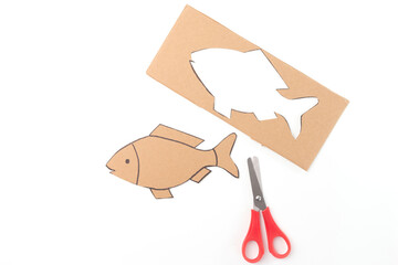 The fish cut out is placed below the cardboard, and the scissors are positioned to the right of the...
