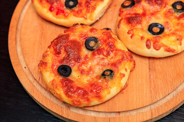 Three small pizzas with olives on top sit on a wooden cutting board