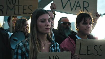 Selective focus on young blonde woman with group of diverse people protesting against war in silence with serious gesture. Different activists with anti-war banners at demonstration for peace outdoors