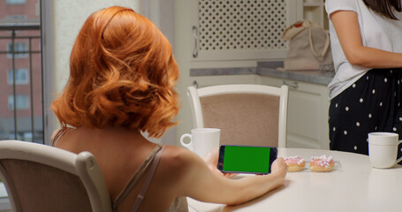 Woman at horizontal phone with green screen not paying attention to her friend talk. Girl is...