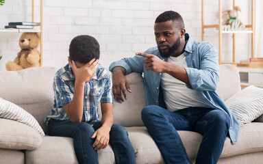 Angry black father scolding stubborn little son for bad behavior at home, boy making facepalm...