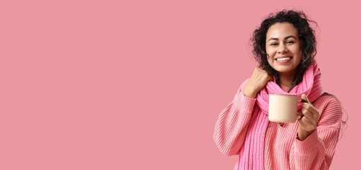 Happy young African-American woman holding mug of hot mulled wine on pink background with space for text