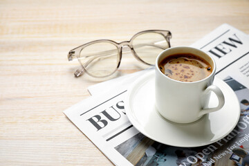Cup of hot coffee with newspaper and eyeglasses on wooden table
