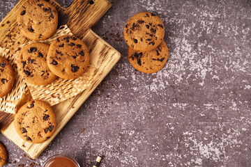 Wooden board of tasty cookies with chocolate chips on grey background