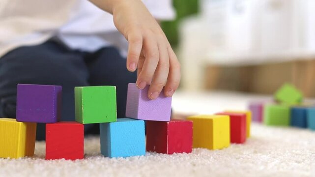 A child builds a wall from colorful wooden eco-friendly cubes. 