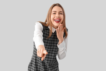 Laughing young businesswoman pointing at viewer on light background. Accusation concept