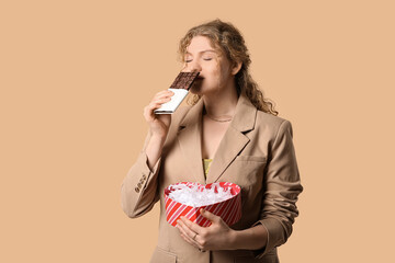 Beautiful young woman with sweet chocolate bar and gift box on brown background