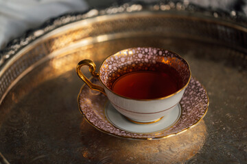cup of black ceylon tea in pink and gold pattern teacup and saucer sitting on silver tray