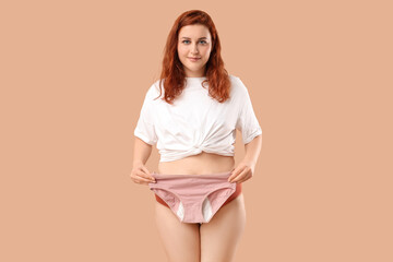 Young woman holding period panties on beige background