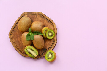 Wooden board with fresh kiwi and mint on lilac background