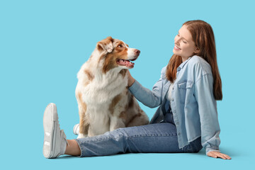 Young woman with cute Australian Shepherd dog sitting on blue background