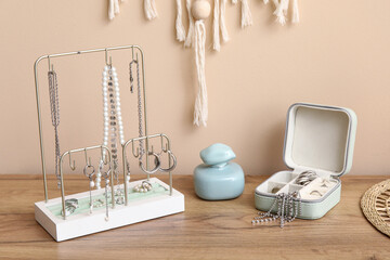 Organizers with stylish different jewelry and perfume bottle on dresser near beige wall
