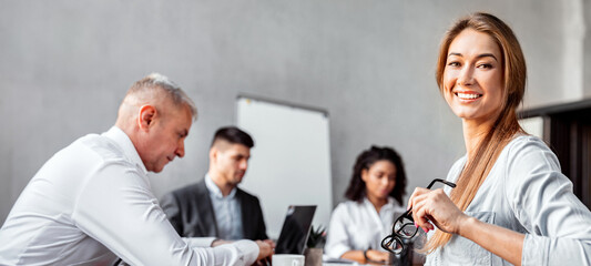 Successful Businesswoman Sitting With Employees At Corporate Meeting Smiling To Camera In Modern Office. Female Entrepreneurship. Free Space