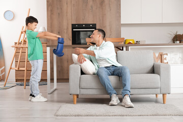 Cute little boy giving boxing gloves to his father in kitchen