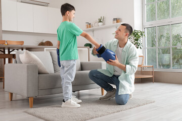 Fototapeta premium Happy father putting boxing gloves on his little son in kitchen
