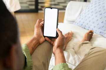 Relaxing at home, African American man using smartphone on couch, copy space