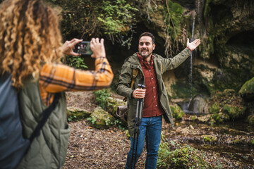 wife take a photo of husband backpacker in front cave in the forest