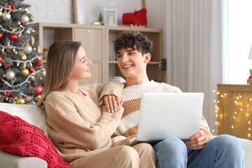 Happy young couple with laptop shopping online at home decorated for Christmas