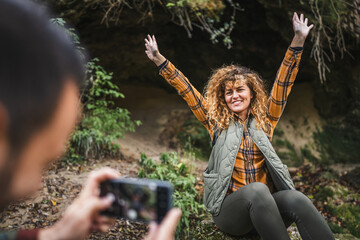 husband take a photo of wife backpacker in front cave in the forest