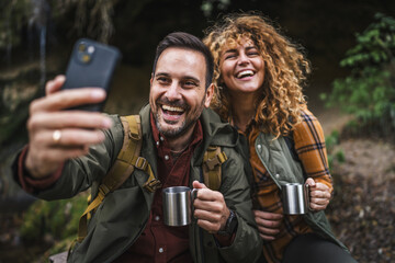 husband and wife hikers sit in front cave and have a video call