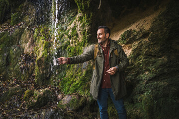 adult man hiker scoop the fresh water into the cup from the waterfall