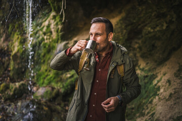 adult man hiker drink the fresh water into the cup from the waterfall