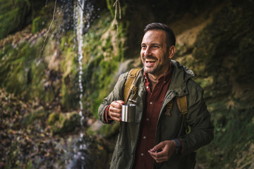 adult man hiker drink the fresh water into the cup from the waterfall