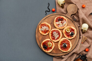 Wooden board with tasty pizzas and decorations for Halloween on dark background