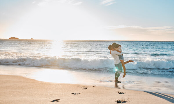 Sunset, couple and kiss with lifting on beach, travel vacation and anniversary holiday for bonding. Summer, man and woman on ocean for carrying, love connection and healthy relationship by seaside