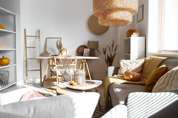 Interior of light living room with grey sofa, pumpkins, workspace and shelving unit