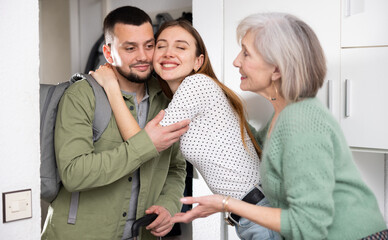 Obraz premium Young adult wife and her elderly mother meeting and embracing husband returning home