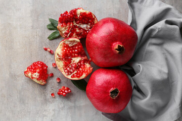 Fresh ripe pomegranates with leaves and seeds on grey background