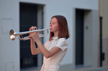 A young woman is playing a trumpet in a city street