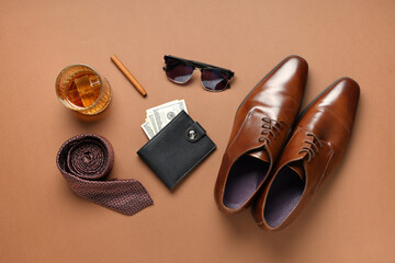 Naklejka premium Stylish men's accessories with shoes and glass of whiskey on brown background