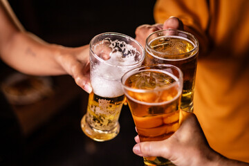 A man's hand and a woman's hand hold beer glasses in a cozy, lively evening party setting. Family and friends gather under the night sky, sharing joyful moments and laughter.