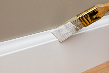 Painting baseboard trim with white paint. Home improvement, remodeling and repair concept.