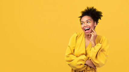 Flirting Girl. Romantic afro woman in yellow dress touching cheek with finger isolated over pink studio wall, copyspace