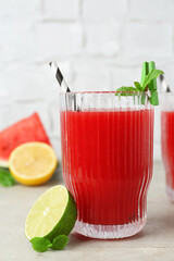 Delicious watermelon drink in glass, fresh fruits and mint on light table, closeup
