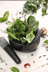 Mortar with different aromatic herbs on white table