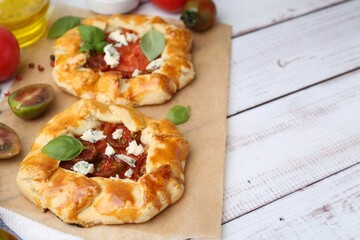 Tasty galettes with tomato, basil and cheese on white wooden table, closeup. Space for text