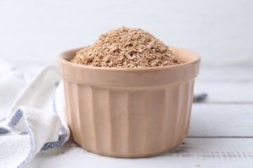 Buckwheat bran in bowl on white wooden table, closeup
