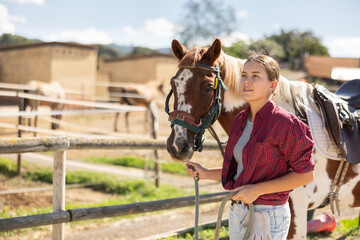 Young woman leading horse by bridle in paddock