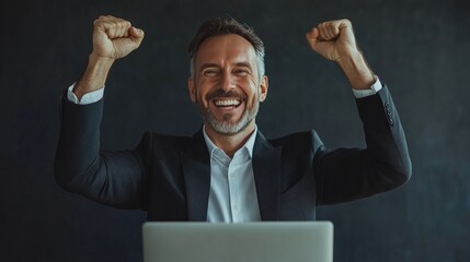 A happy businessman with his laptop is celebrating success, he has raised hands up in the air and smiling to camera