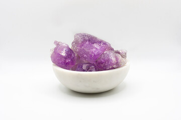 A isolated image of a bowl full of unpolished amethyst crystals on a white background. 